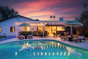 A pool area with lounge chairs and umbrellas, a covered patio, and a house with a white exterior. - Epic Desert Stay | Pool, Hot Tub & Sports Court (Scottsdale)