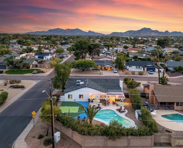 A residential area with a house featuring a swimming pool, a tennis court, and a patio area with outdoor furniture. - Desert Social Club | Pool • Hot Tub • Sports Court (Scottsdale)