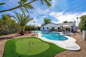 A backyard with a swimming pool, a patio area, and a small lawn with a flagstick. - Epic Desert Stay | Pool, Hot Tub & Sports Court (Scottsdale)