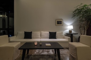 A living room with a white sofa, two black cushions, a coffee table, a lit candle, a small bowl, and a framed picture on the wall. - Thanks Hotel (Xinzhou)
