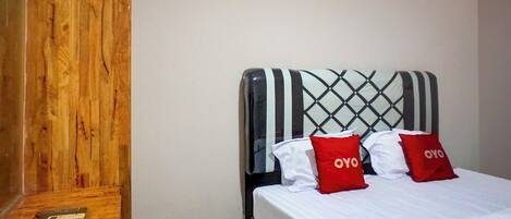 A hotel room with a wooden wardrobe, a bed with a striped headboard, and two red pillows with the word "OYO" on them.