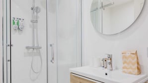 A modern bathroom with a glass-enclosed shower, a round mirror, and a white sink with toiletries. - Modern "green Suites" Residence - Meudon/valizy (Meudon)