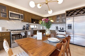 Uma cozinha moderna com armários de madeira, eletrodomésticos de aço inoxidável, uma mesa de jantar de madeira posta para quatro pessoas e um vaso decorativo com flores.