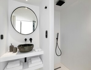A bathroom with a round mirror, a stone sink, and a handheld showerhead.
