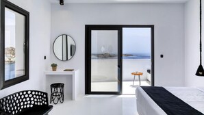 Une chambre moderne avec un lit, un bureau, une chaise, un miroir et une vue sur la mer, visible à travers une porte coulissante.