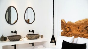 Une salle de bain moderne avec deux miroirs ovales, une tête de lit en bois, un grand lavabo en forme de bol en bois et un luminaire suspendu.
