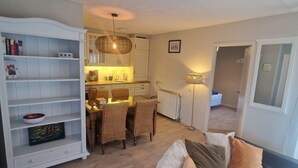 A living room with a sofa, a dining area with a table and chairs, a kitchen with cabinets and a hanging light fixture. - Seagull Bungalow Park Sollasi (Noordwijkerhout)