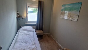 A narrow room with a bed, a small table, and a window with curtains. - Seagull Bungalow Park Sollasi (Noordwijkerhout)