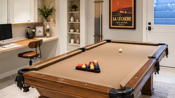 A pool table with balls, a chair, a desk with a computer, shelves with decorative items, and a door with a poster.