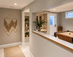 A pool table in a room with a neutral color scheme, a decorative wall hanging, and a potted plant.