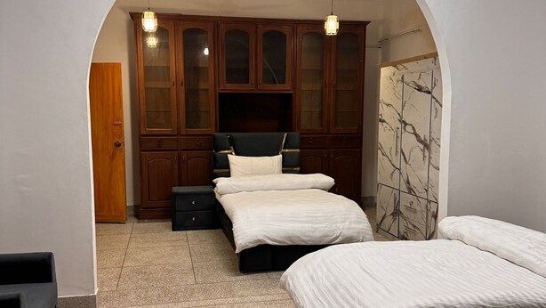 A bedroom with three beds, wooden cabinets, and a tiled floor. - Taj Villa (Islamabad)