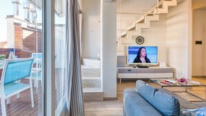 Ein modernes Wohnzimmer mit einer Couch, einem Couchtisch und einem Fernseher. Eine Treppe führt zu einer oberen Etage.