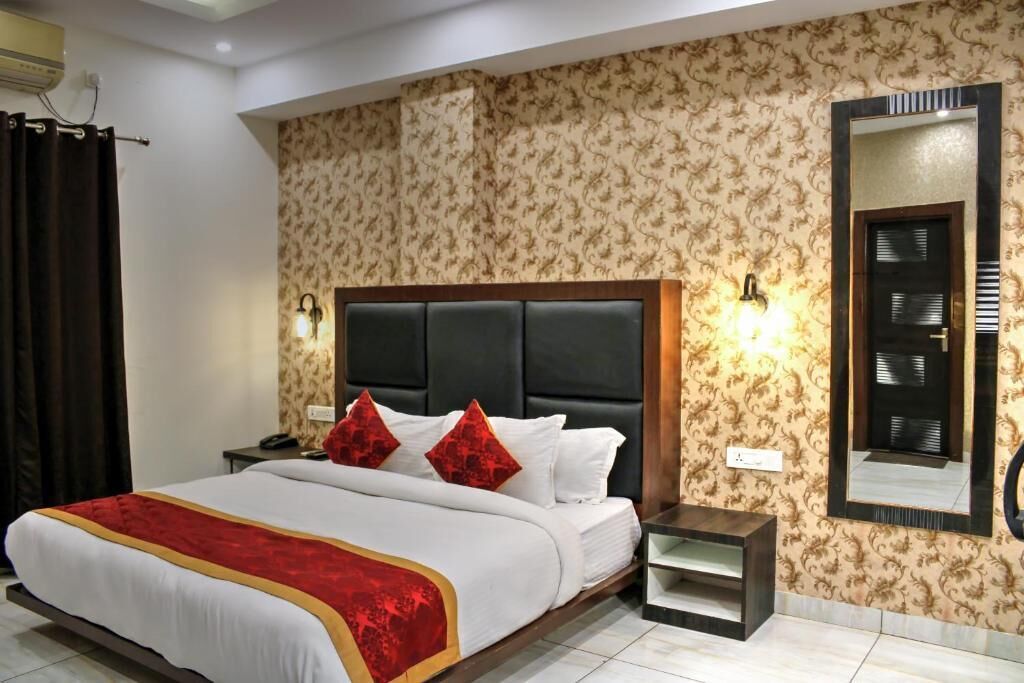 Habitación de hotel con una cama grande, cabecera, dos mesitas de noche, un espejo y papel tapiz estampado.