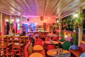 An indoor restaurant with wooden tables and chairs, a bar area, and hanging plants. - Hotel Hill View (Dehradun)