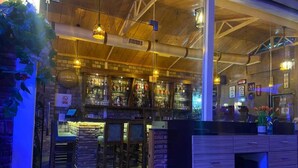 A bar area with wooden ceiling beams, hanging lights, and a brick wall. - Hotel Hill View (Dehradun)