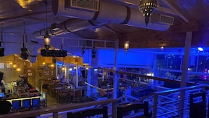 An interior view of a restaurant with a bar area, seating, and a view through large windows. - Hotel Hill View (Dehradun)