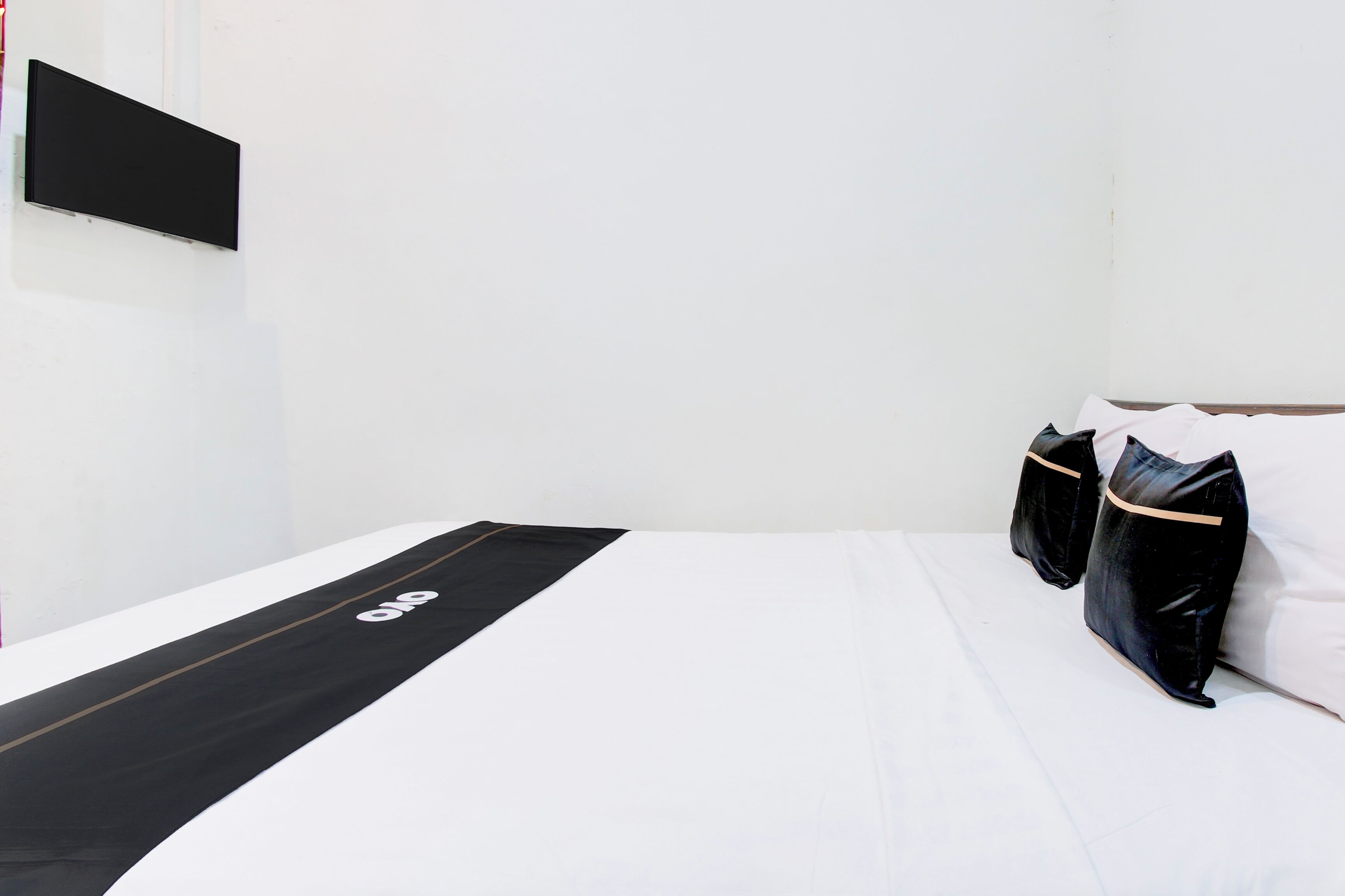 A minimalist hotel room with a bed, a black runner with a logo, and two black pillows.