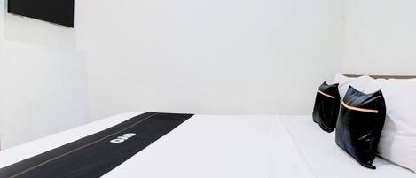 A minimalist hotel room with a bed, a black runner with a logo, and two black pillows.