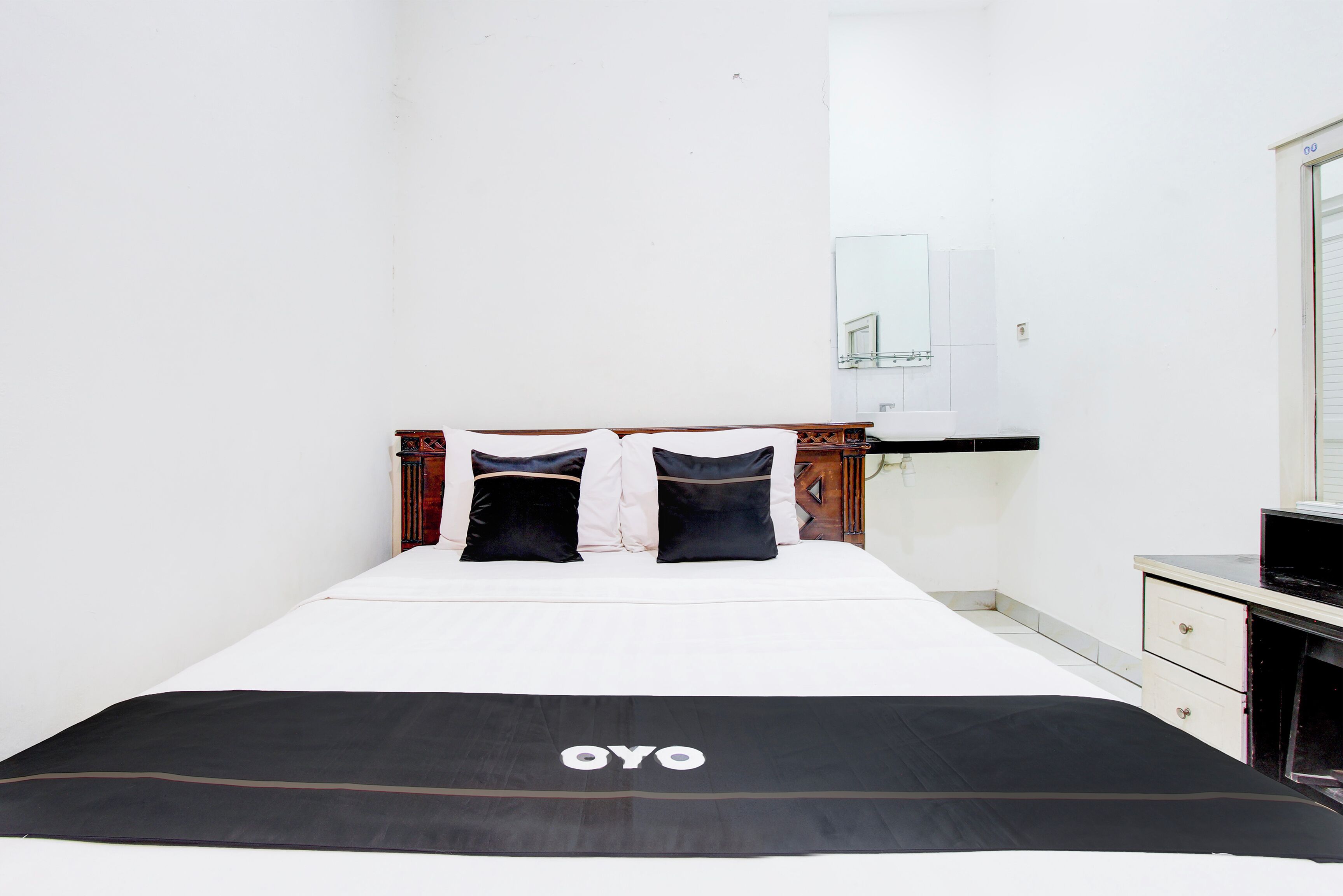 Een opgemaakt bed met een zwart-wit deken, een houten hoofdbord en twee zwarte kussens.