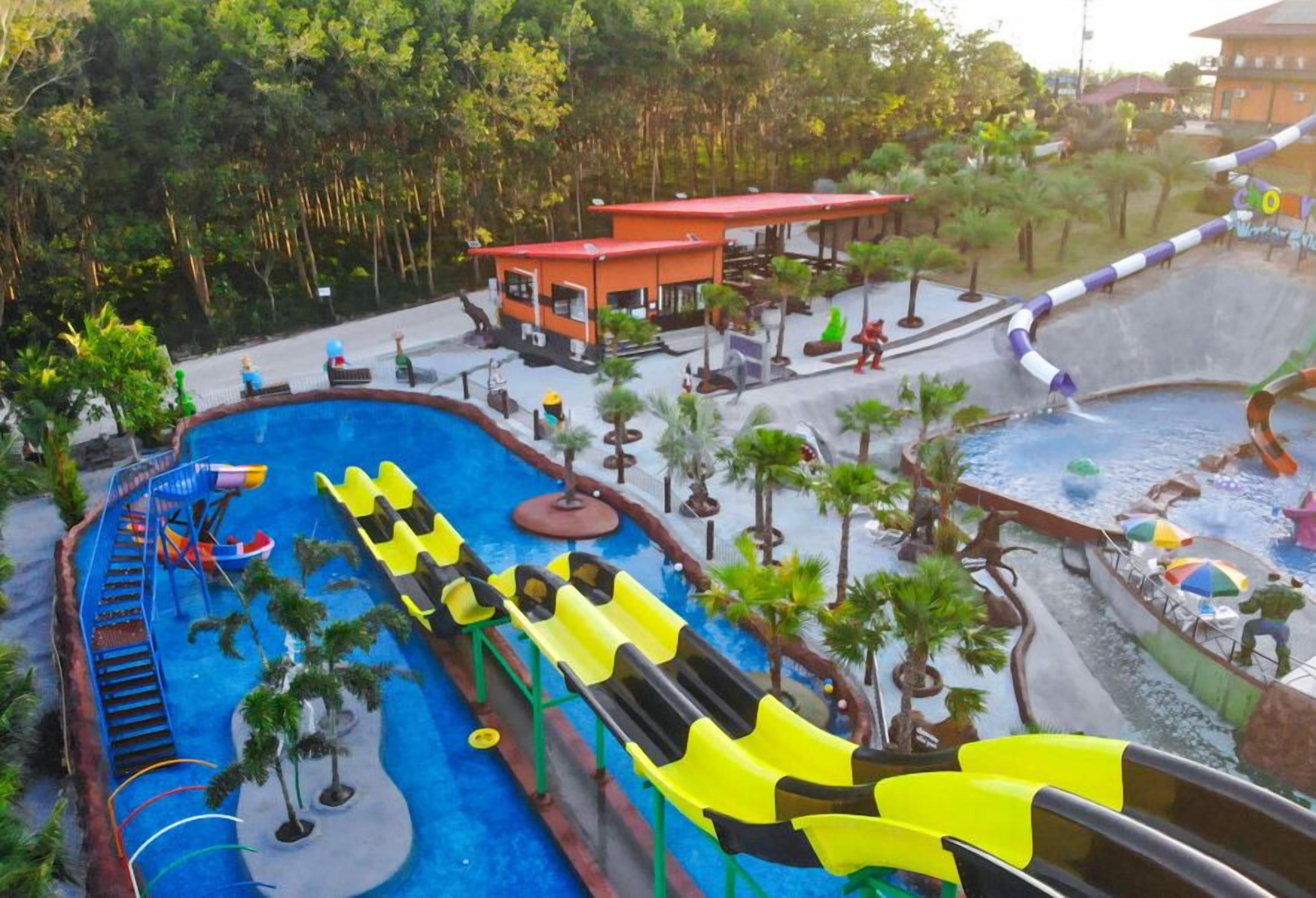 Waterpark met meerdere glijbanen en zwembaden, omringd door palmbomen en een klein gebouw.
