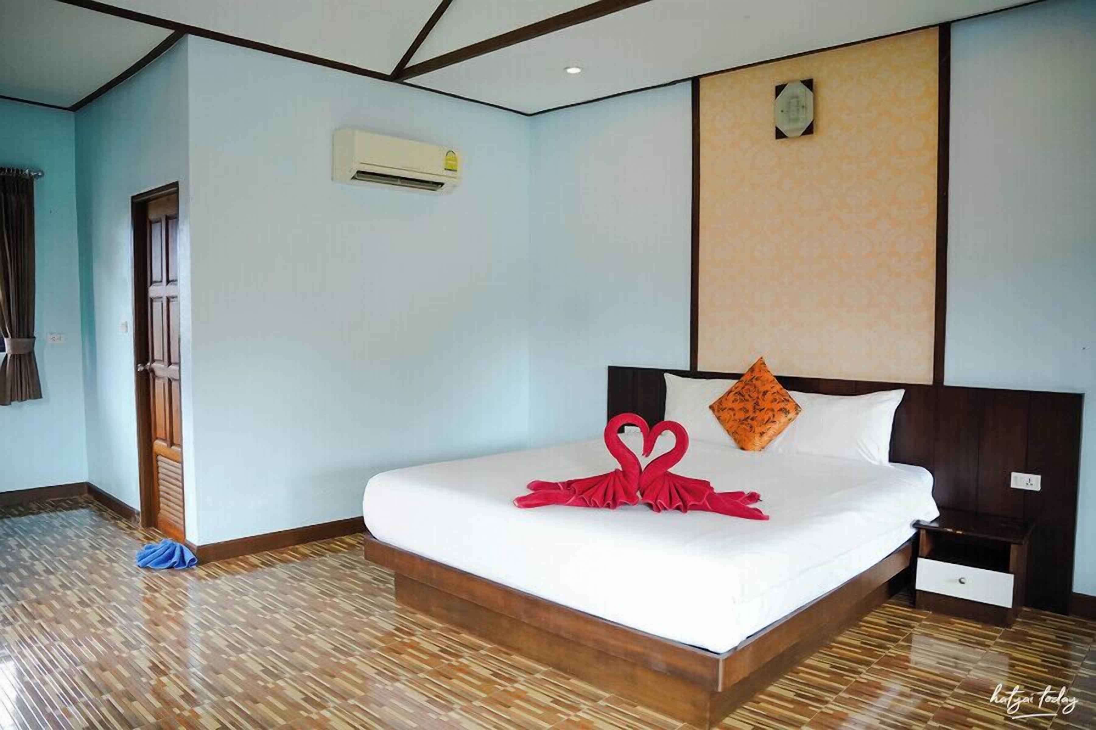 Una habitación de hotel con una cama grande, piso de madera, un equipo de aire acondicionado y una mesita de noche.