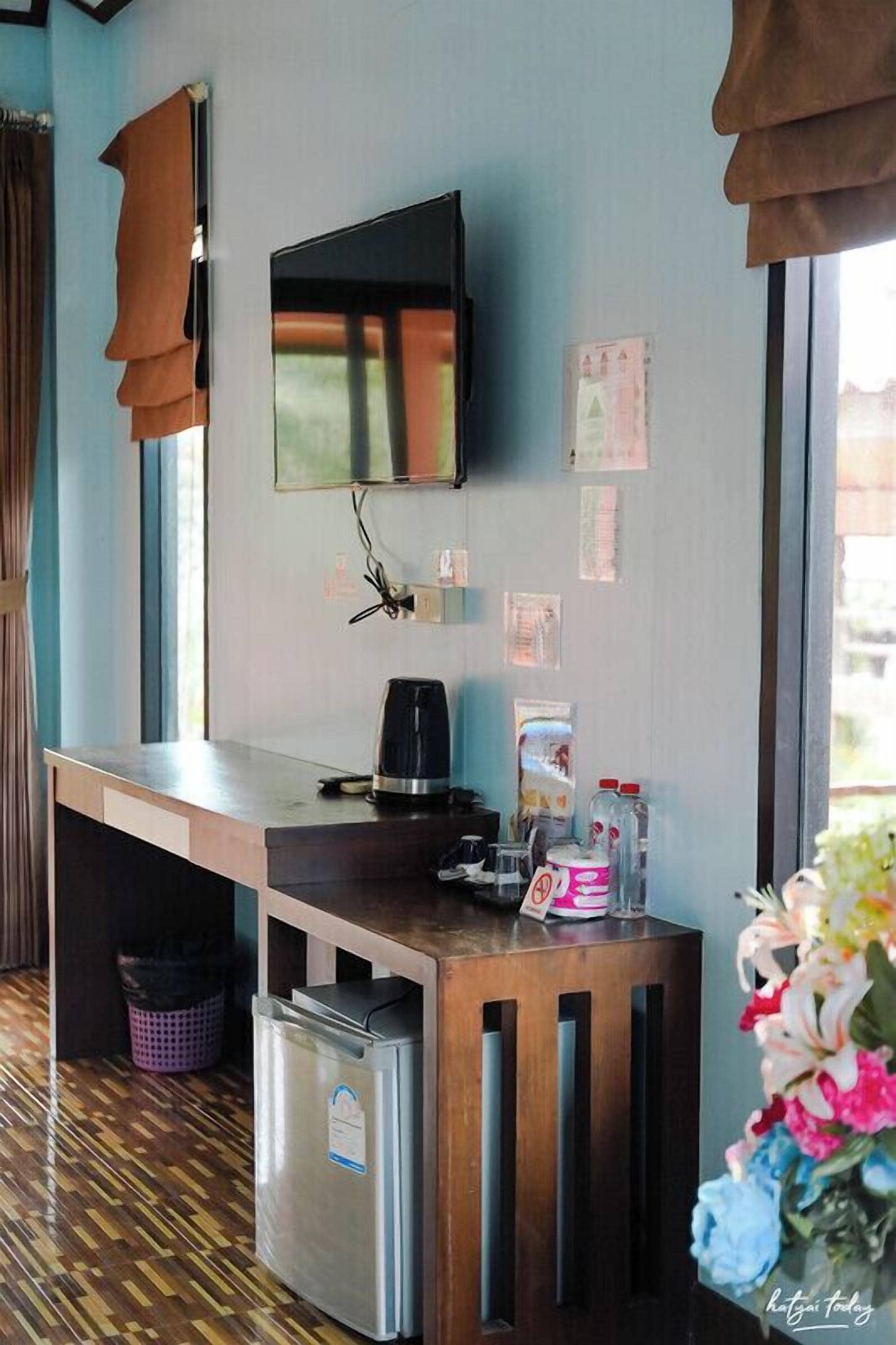 Une chambre d’hôtel avec un bureau en bois, un téléviseur fixé au mur, un petit réfrigérateur et une poubelle.