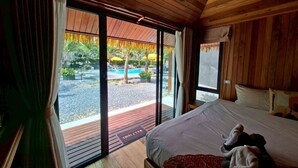 Camera da letto con un letto grande, soffitto in legno e vista su un'area piscina all'aperto.