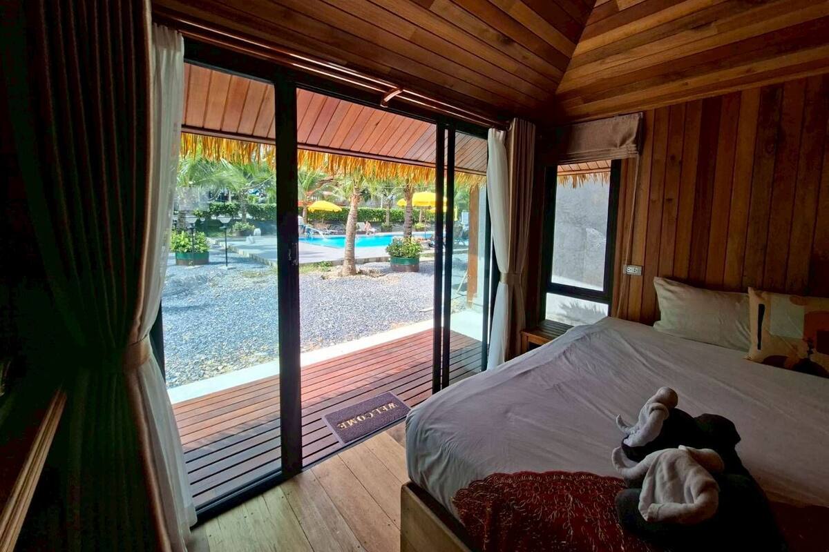 Une chambre dotée d’un grand lit, d’un plafond en bois et donnant sur une piscine extérieure.