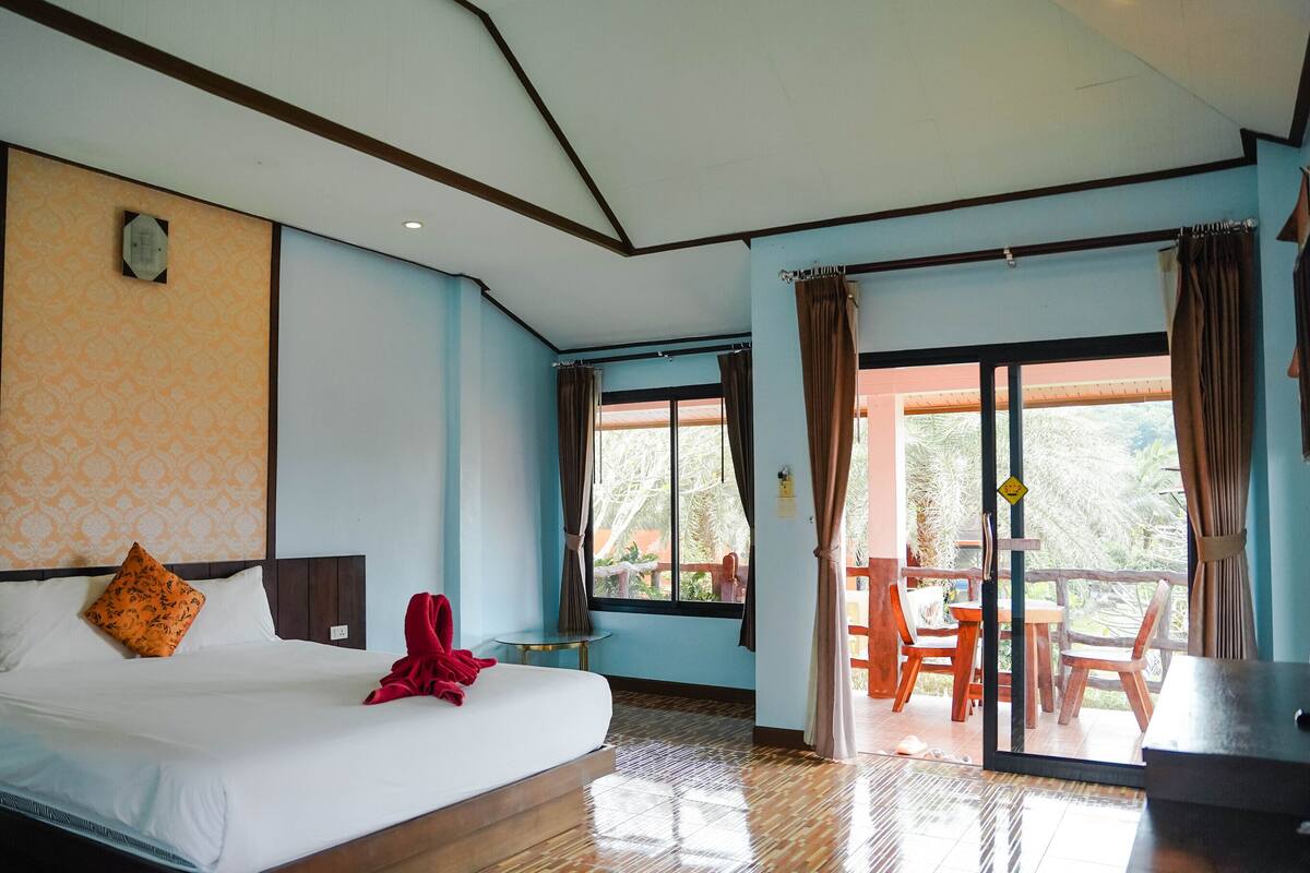 Une chambre d’hôtel avec un grand lit, une petite table et un balcon équipé de chaises en bois.