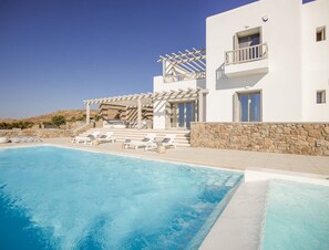 Eine moderne Villa mit Swimmingpool, Sitzgelegenheit im Freien und einer Steinmauer.