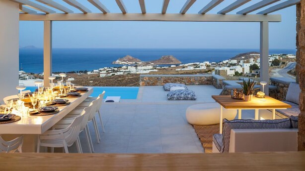 An outdoor dining area with a view of the sea and a white building complex. - Nice Villa at Kalafatis Beach (Mykonos)