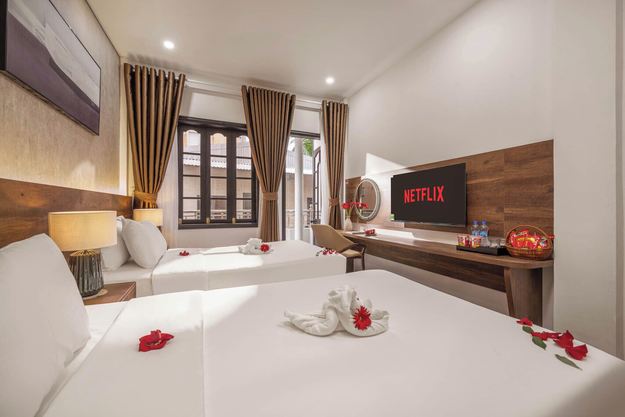 A hotel room with two beds, a desk, a TV, and a window with curtains.
