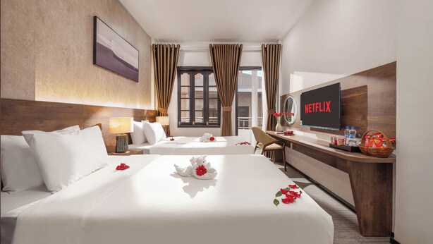 Een hotelkamer met twee bedden, een bureau met een televisie en uitzicht op buiten.