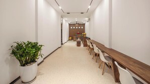 Een moderne hotellobby met een lange houten receptiebalie, witte stoelen en een potplant.