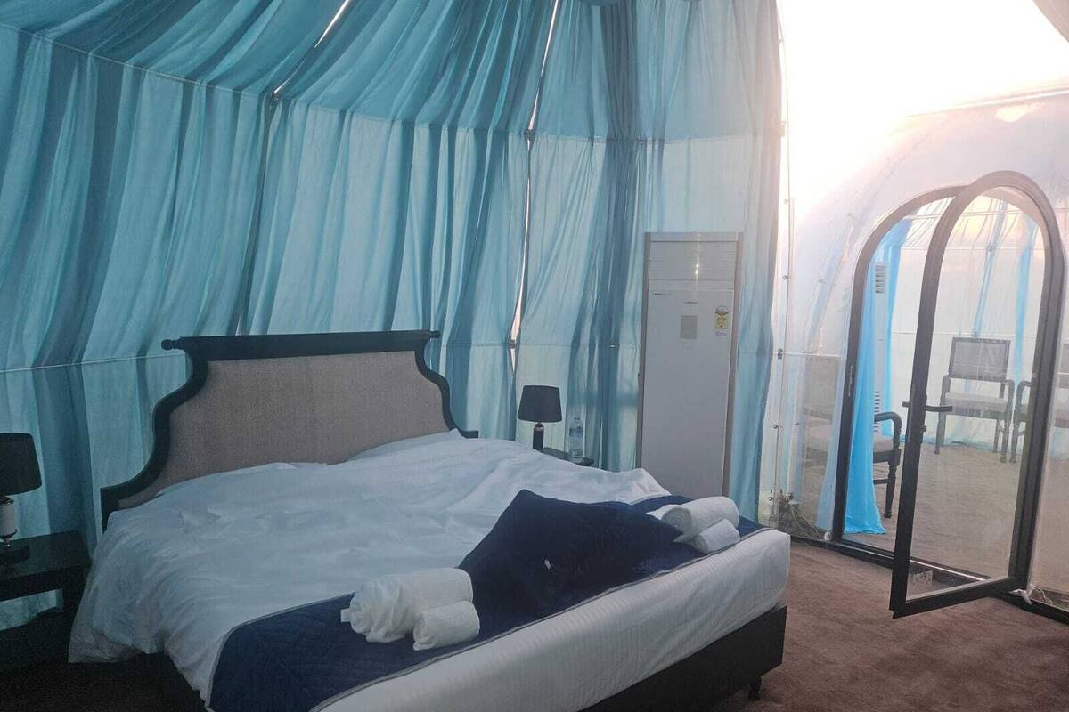 A bedroom with a bed, a nightstand, a lamp, and a door leading to an outdoor area.