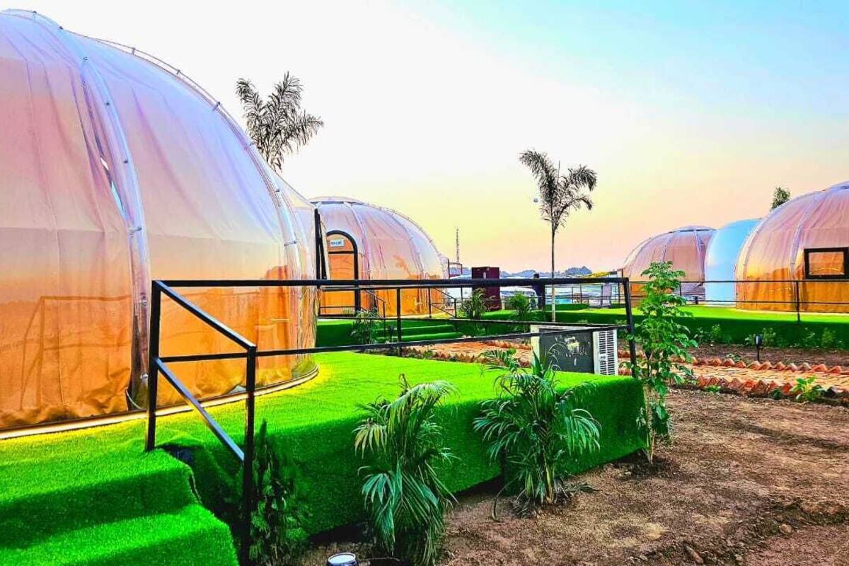 A series of dome-shaped structures with transparent walls, surrounded by green artificial grass and palm trees.