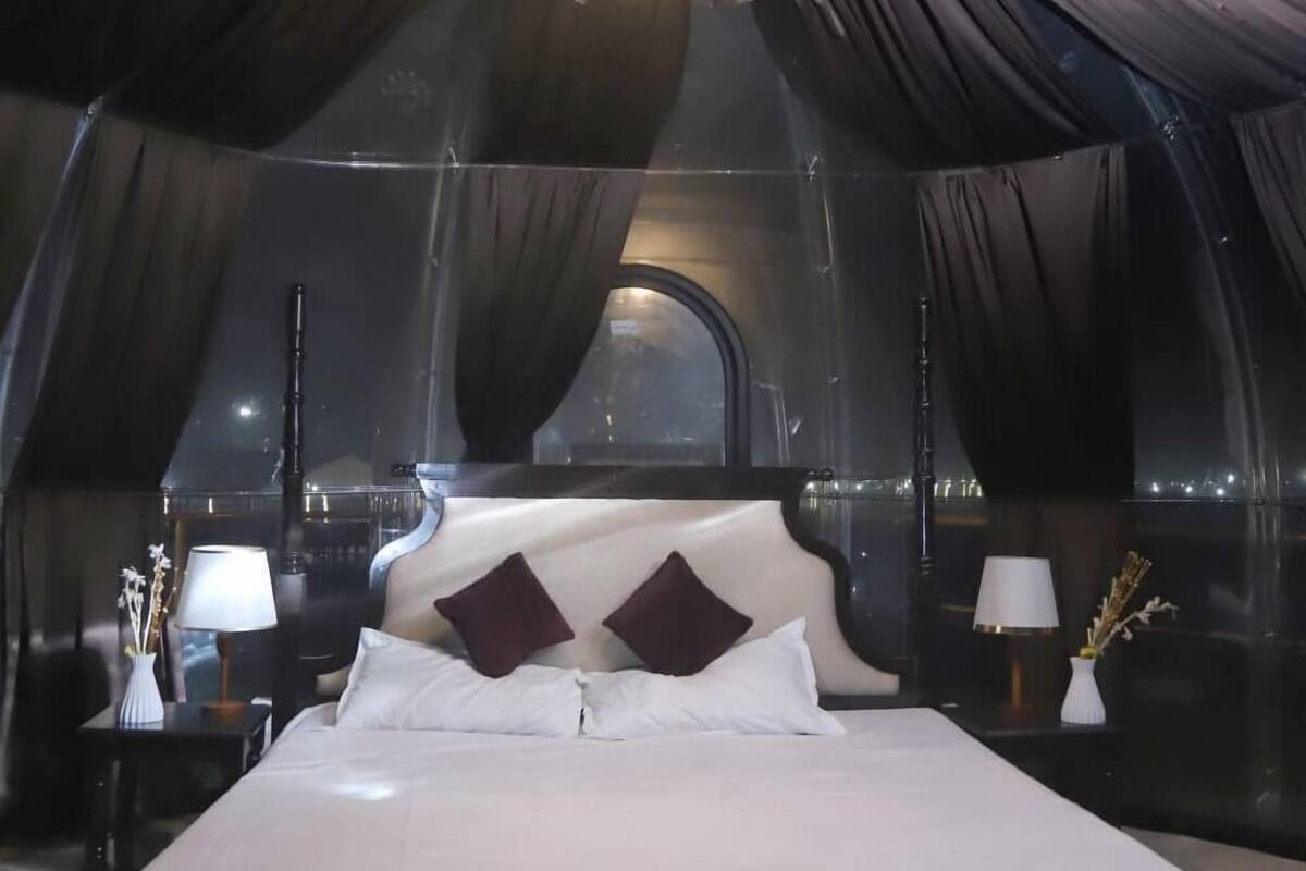 A luxurious bedroom with a large bed, dark drapes, and a chandelier.