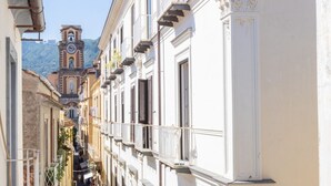 A narrow street with buildings on either side, a clock tower in the distance, and a mountain backdrop. - Charming bedroom in Sorrento with balcony (Sorrento)