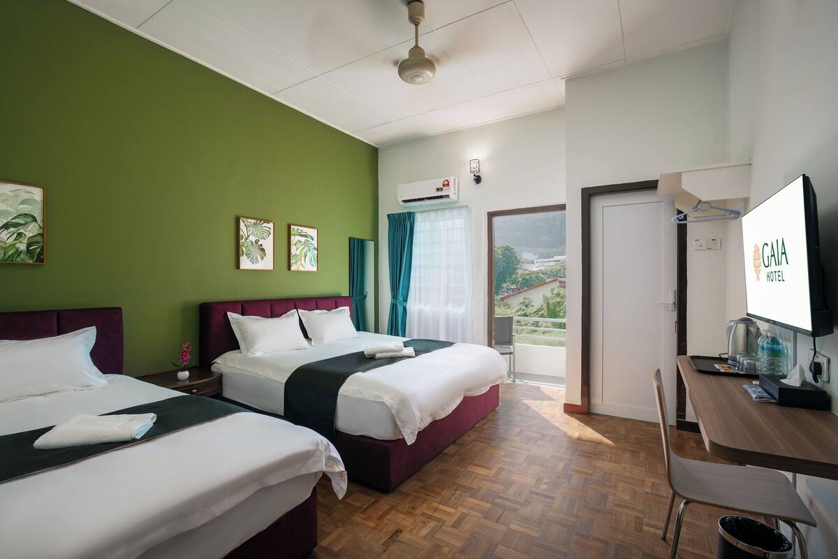 A hotel room with two beds, a desk, a TV, and a balcony with a view.