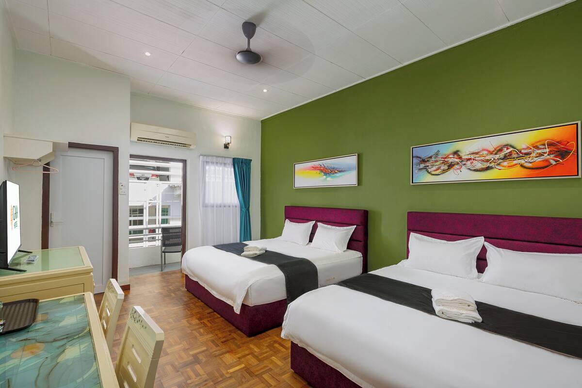 A hotel room with two beds, a desk, a TV, and a view of the outside.
