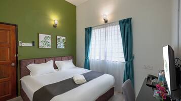 A hotel room with a bed, a desk with a computer, a chair, a window with curtains, and wall-mounted lights.