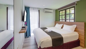 A hotel room with a large bed, a bedside table, a TV, and a window with curtains. - GAIA Hotel (George Town)