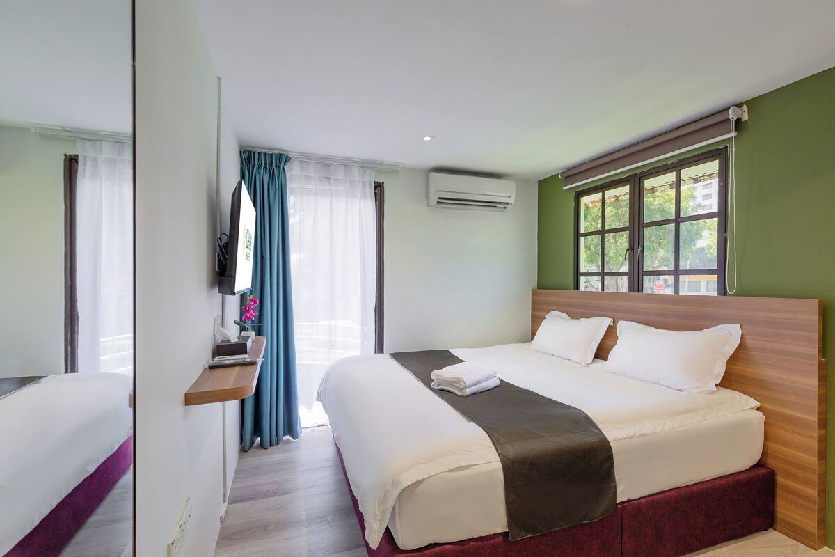 A hotel room with a large bed, a bedside table, a TV, and a window with curtains.