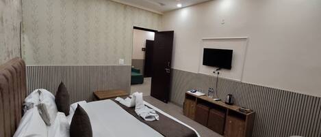 A hotel room with a bed, bedside table, TV, and a desk with a chair.