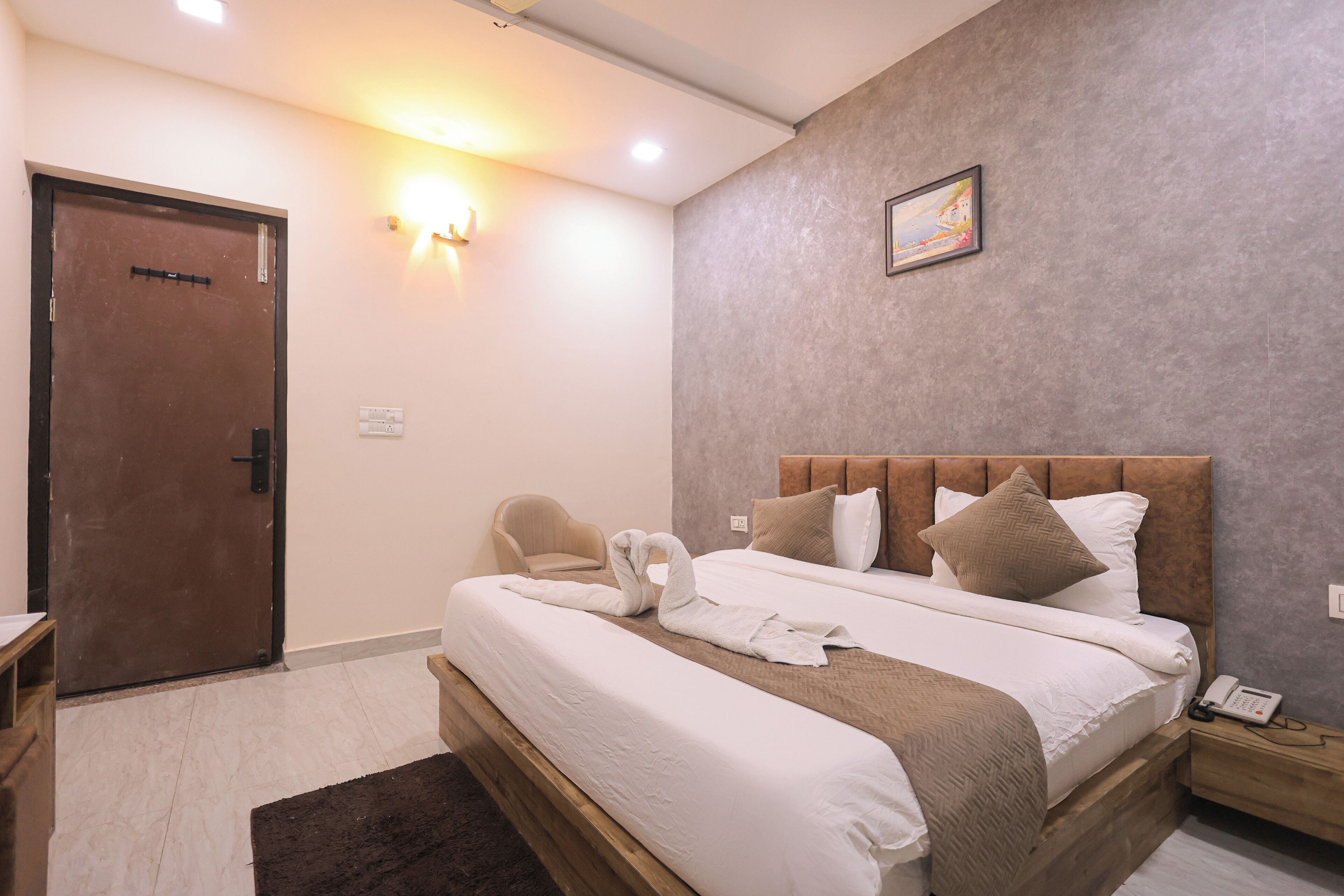 A hotel room with a large bed, a wooden headboard, a wall-mounted light, and a door.