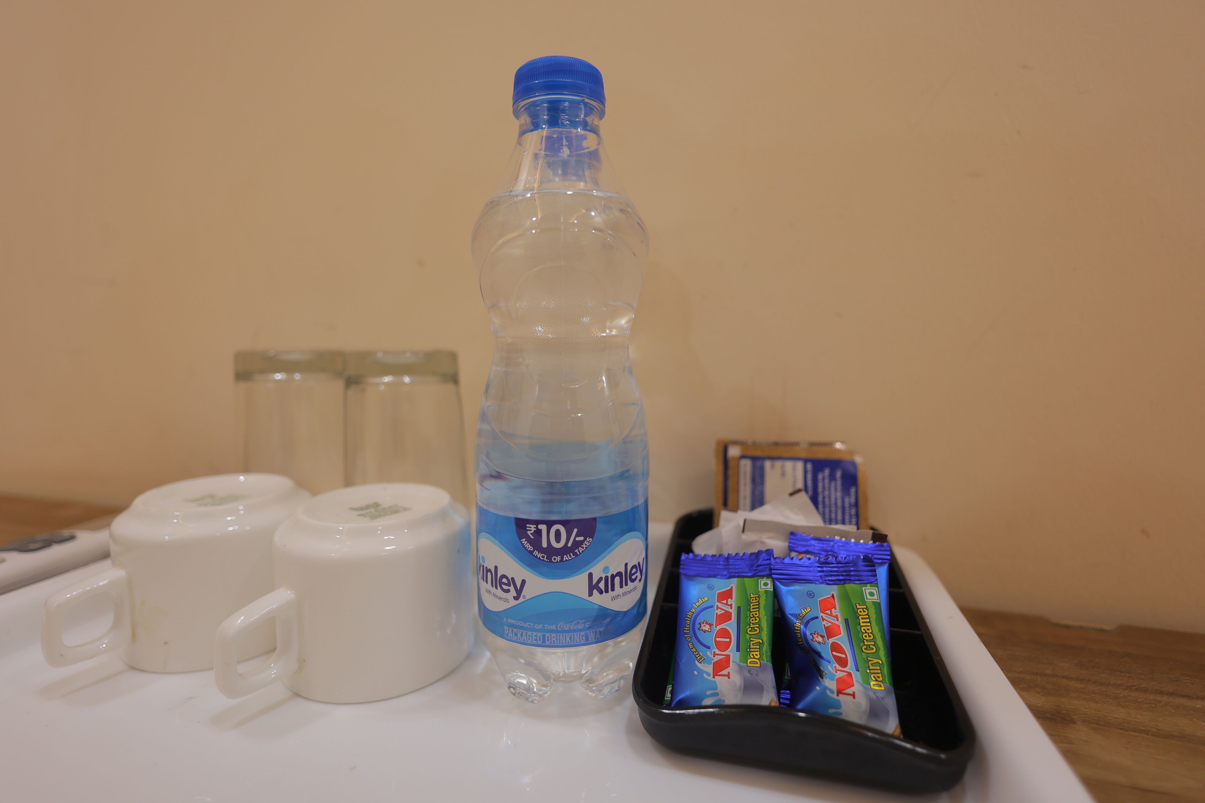 A table with a bottle of water, two cups, and packets of NOVA dairy creamer.