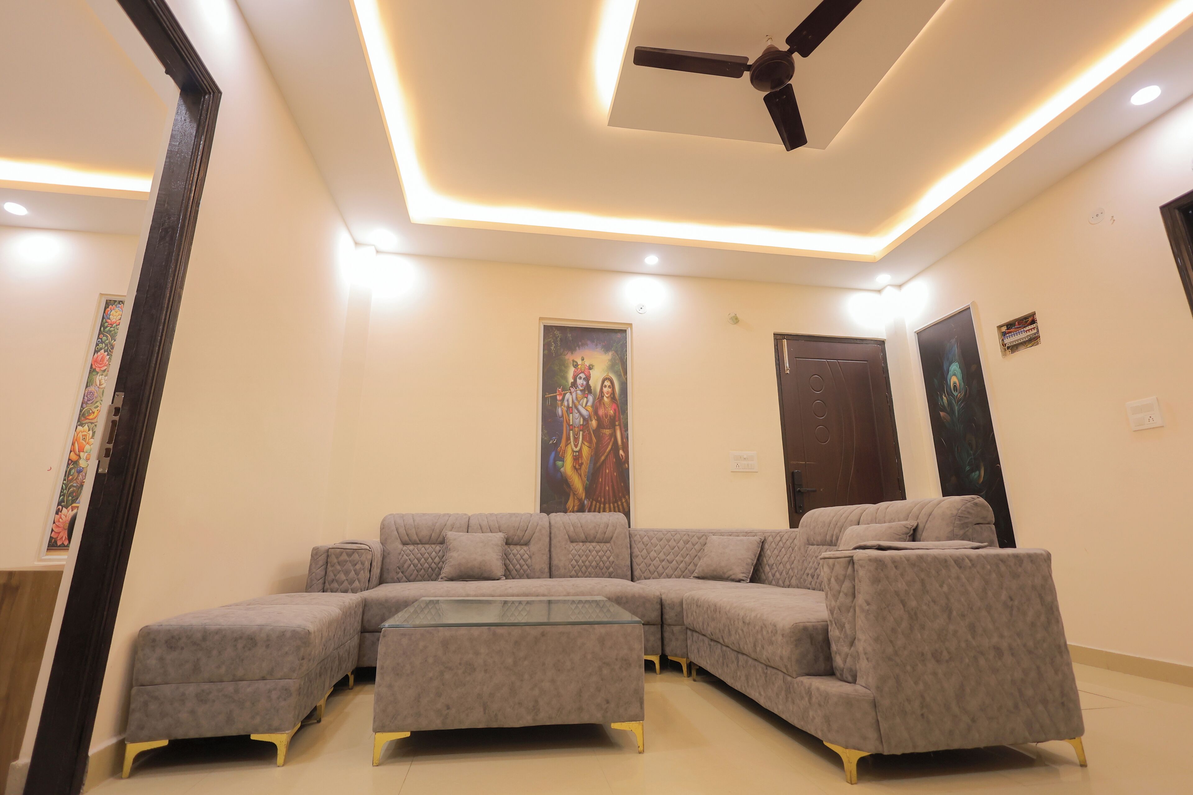 Ein modernes Wohnzimmer mit Ecksofa, Deckenventilator, Einbauleuchten und Kunstwerken an den Wänden.