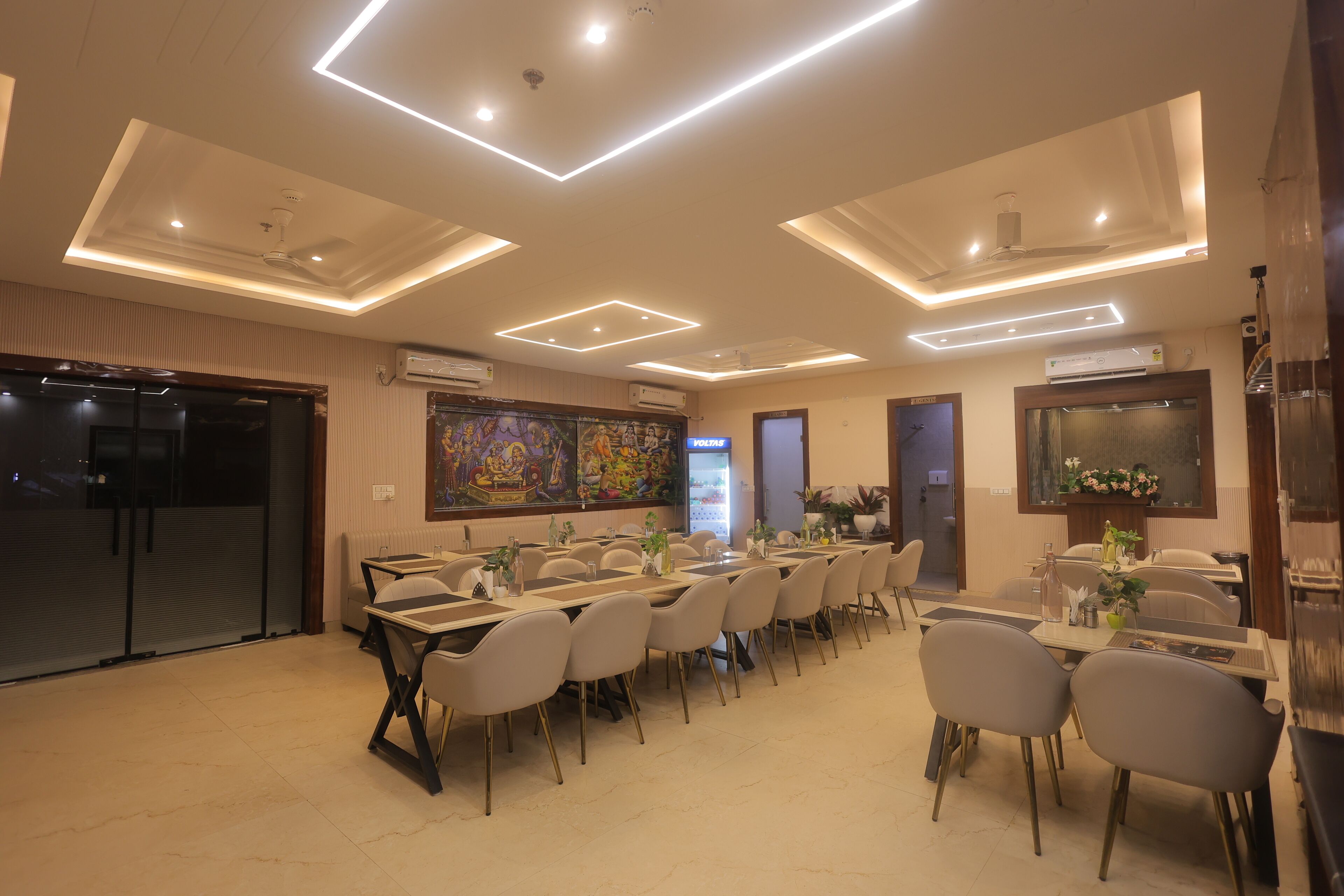 A conference room with a long table, multiple chairs, ceiling lights, and a large painting on the wall.