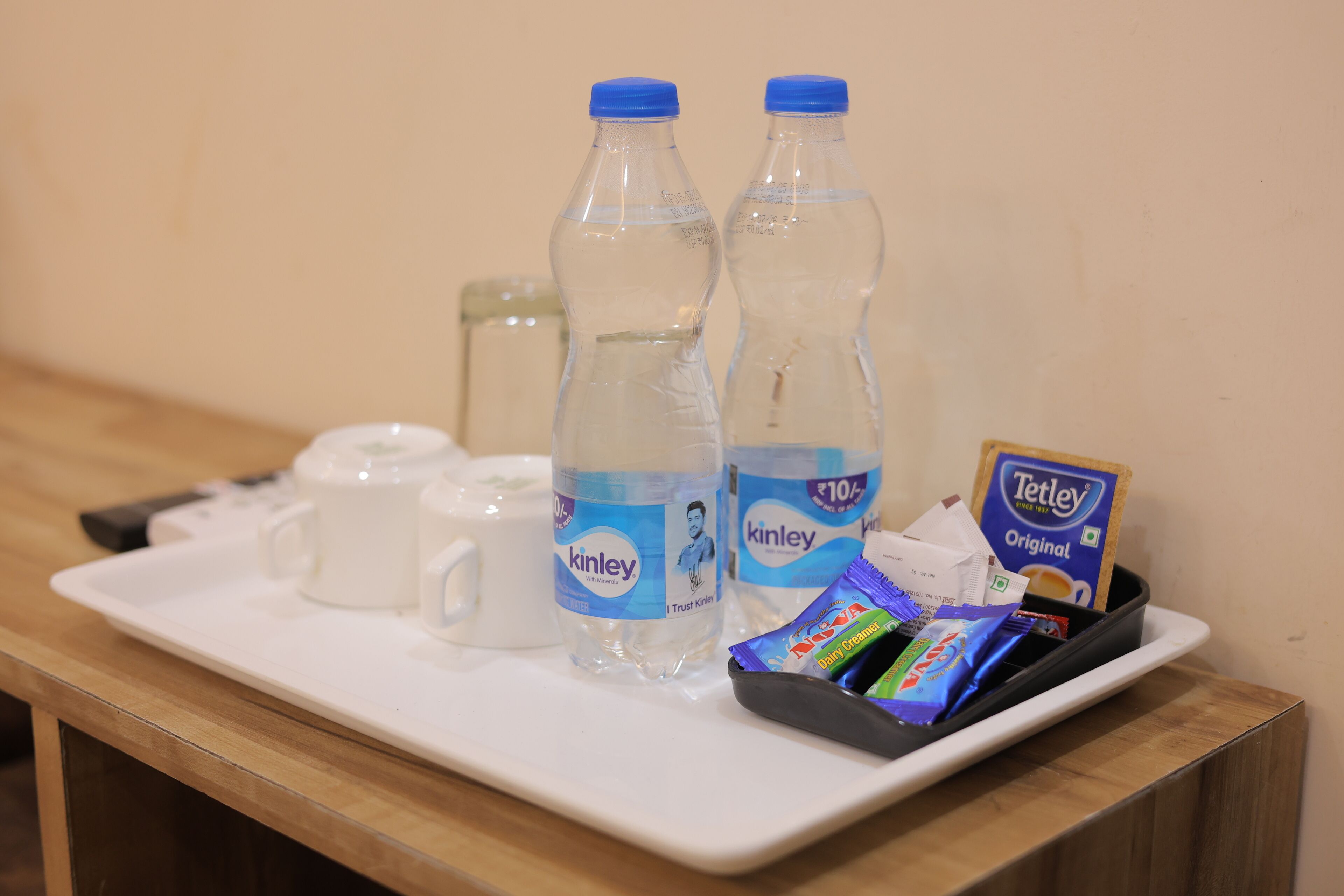 A tray with two bottles of Kinley water, a Tetley tea packet, a small packet of Dove body lotion, and a white mug.