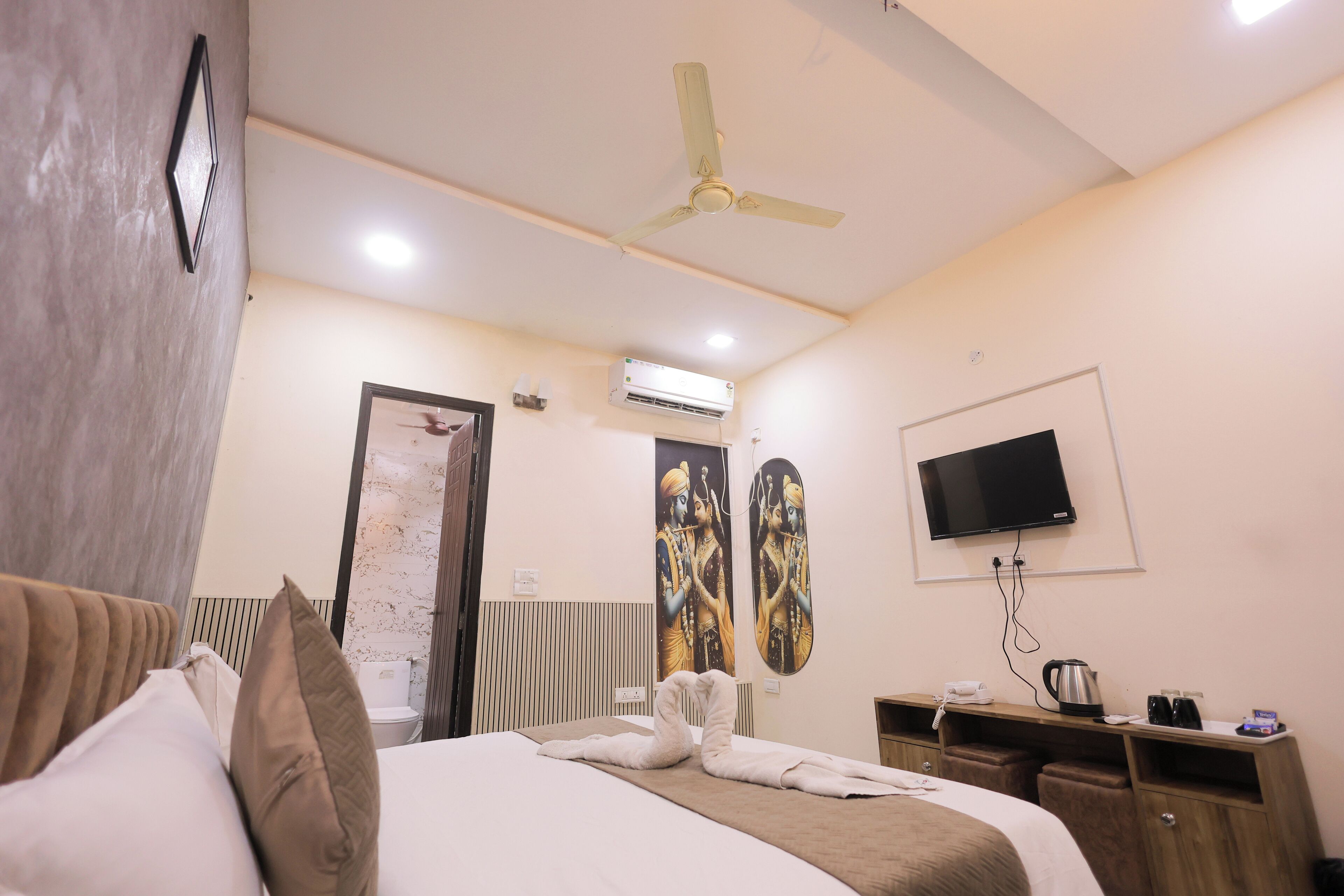 Una habitación de hotel con cama, ventilador de techo, aire acondicionado, televisión y minibar.